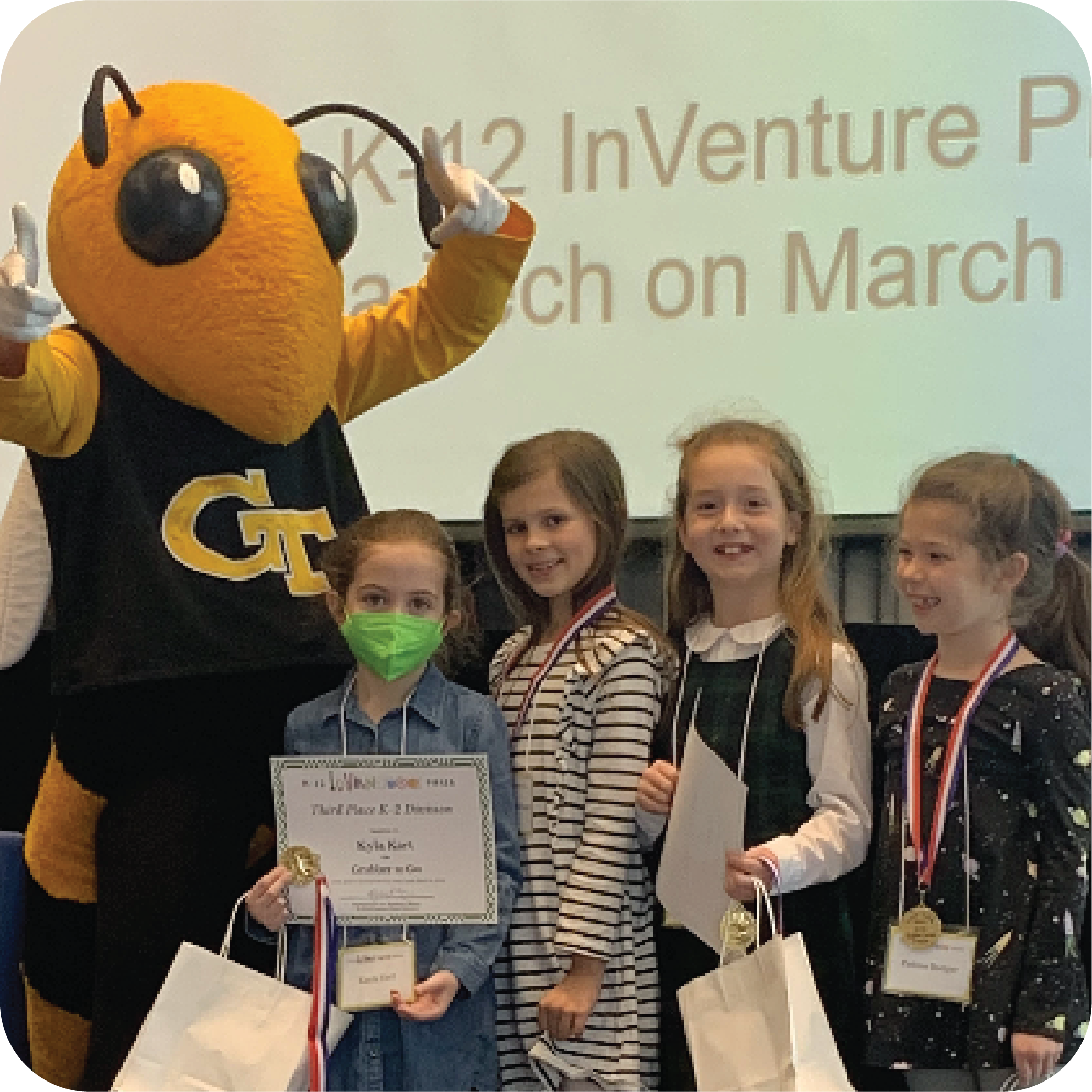Four smiling students holding certificates and standing next to Buzz (Georgia Tech's yellowjacket mascot).